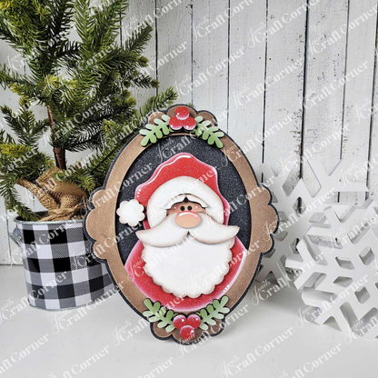 A festive scene features a potted pine, Janet's Craft Corner Framed Santa Shelf Sitter, and a white snowflake ornament on a white wooden surface with a plaid pot—perfect for charming seasonal home decor.