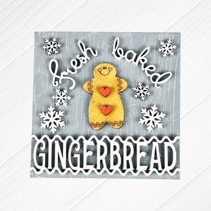 Janet's Craft Corner Gingerbread Squares feature a smiling gingerbread cookie, red heart buttons, and white snowflakes on gray wood with "fresh baked GINGERBREAD" in playful white text. Perfect DIY seasonal decor or for Swappable Square Displays.