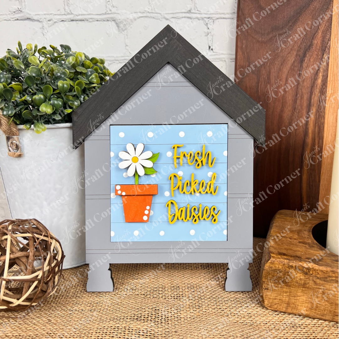 The Bloom & Grow Squares by Janet's Craft Corner is a decorative house-shaped wood sign kit with a flowerpot and daisy design, perfect for tiered tray decor on tables or shelves.