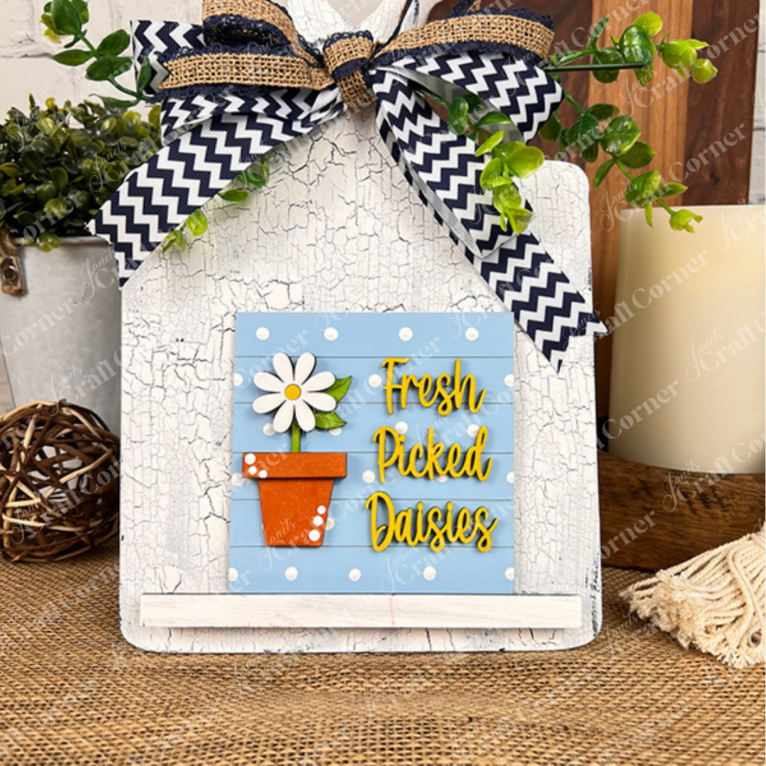 The Bloom & Grow Squares by Janet's Craft Corner is a decorative white wood sign kit with a chevron ribbon, greenery, and a "Fresh Picked Daisies" plaque—perfect for adding charm to your tiered tray or rustic table decor.