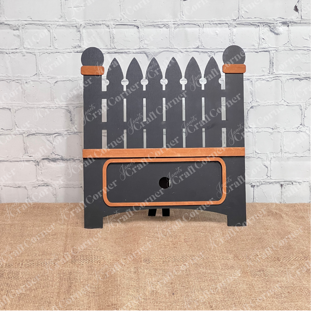 Janet's Craft Corner Garden Fence Interchangeable Base DIY home decor kit  shown painted black with stained accents  in front of a white brick wall.