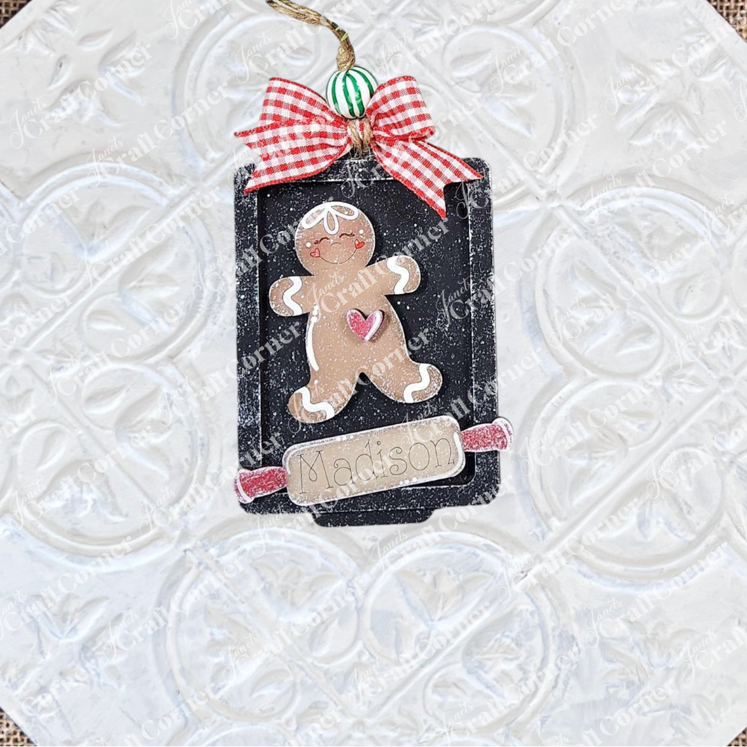 A black gift tag ornament with a gingerbread figure, pink heart, red gingham bow, and "Madison" on a silver label—part of Janet's Craft Corner Gingerbread Ornaments DIY holiday craft kit set of 8. Perfect festive décor!.