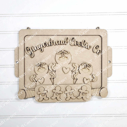 The Gingerbread Cookie Sheet Sign by Janet's Craft Corner is a DIY seasonal home decor craft kit featuring raised gingerbread figures and "Gingerbread Cookie Co." text, perfect holiday wall decoration for shiplap backgrounds.
