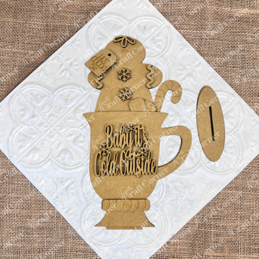 Janet's Craft Corner Gingerbread Hot Cocoa Mug Shelf Sitter DIY craft kit features a brown paper cutout mug with “Baby It’s Cold Outside,” gingerbread figure, candy cane, marshmallows, and snowflakes—perfect festive décor for your home.