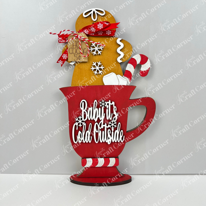The Gingerbread Hot Cocoa Mug Shelf Sitter DIY kit from Janet's Craft Corner features a festive red mug with "Baby It's Cold Outside," gingerbread hot cocoa cookie, candy cane, snowflakes & tag—ideal for charming holiday shelf decor.