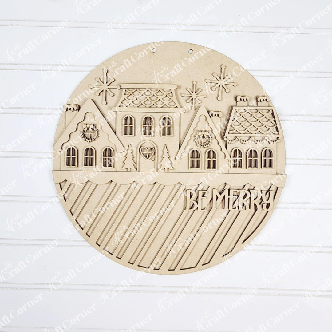 Janet's Craft Corner Gingerbread Village Door Hanger features engraved snowy houses, snowflakes, stars, and diagonal stripes with "BE MERRY!"—a festive décor or DIY craft kit to brighten your holidays.