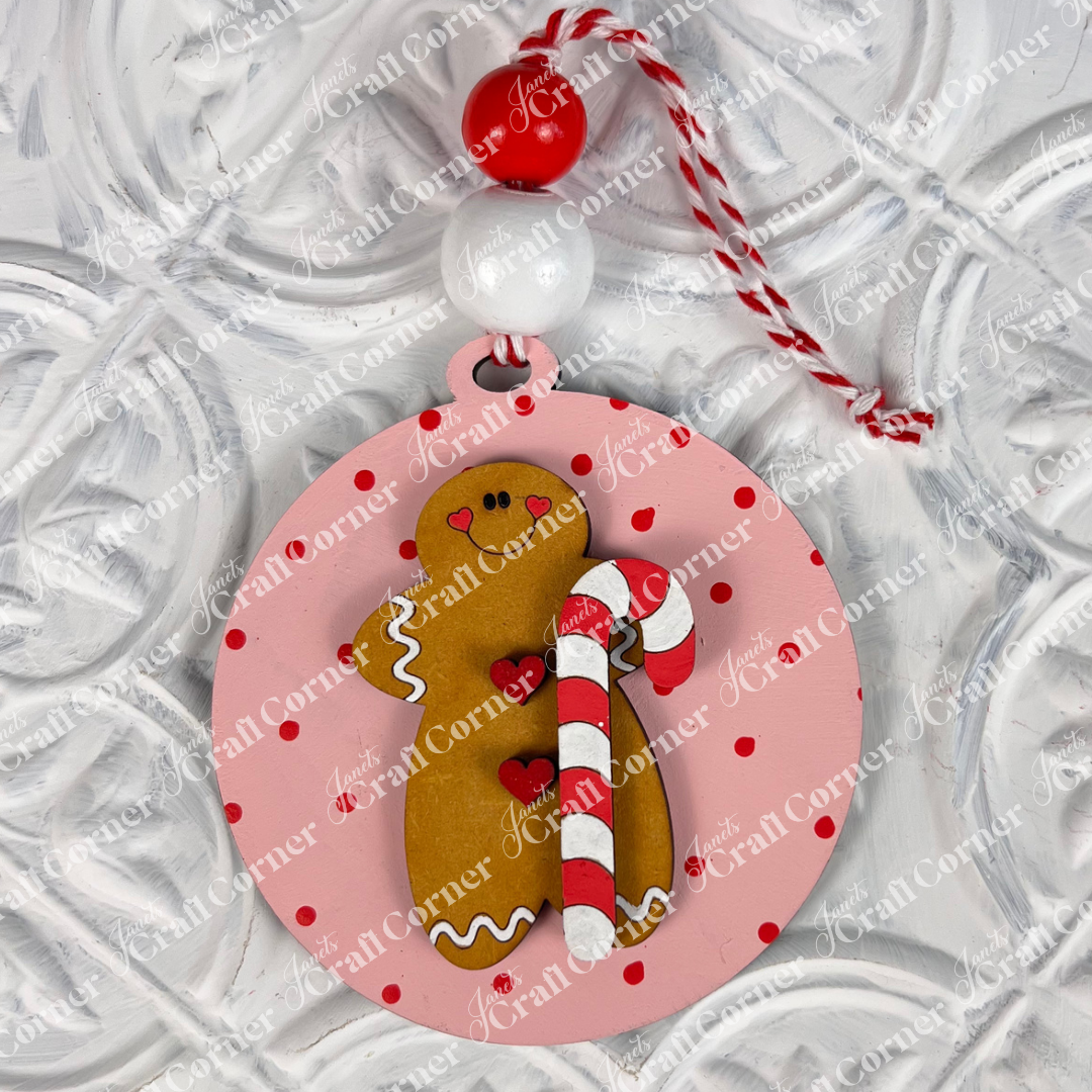 Add a charming touch to your home décor with the Round Christmas Ornaments from Janet's Craft Corner. This captivating ornament features a round pink design adorned with red polka dots and showcases a cheerful gingerbread figure holding a candy cane. Accented with red and white beads and finished with a striped hanger, it beautifully complements any textured white background.