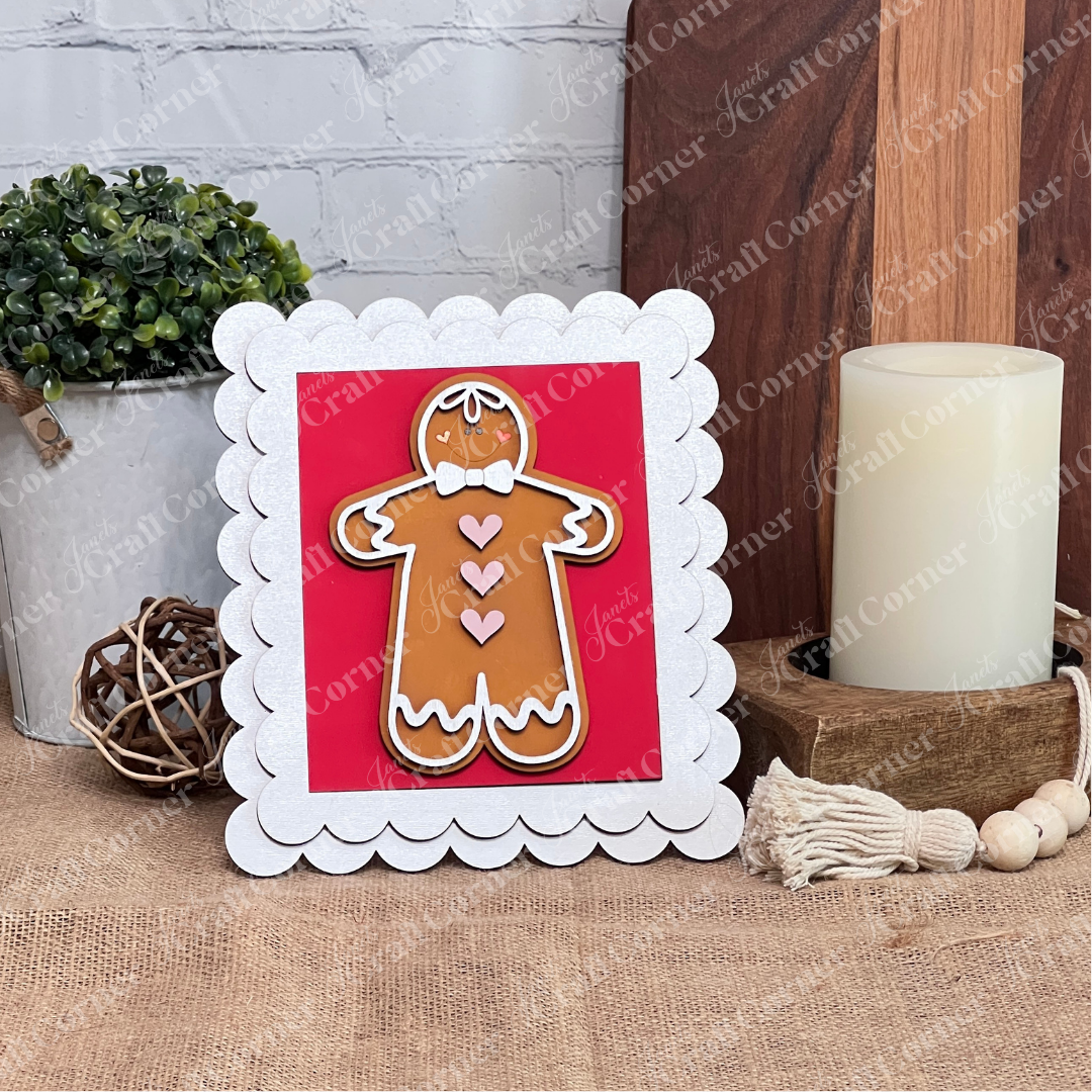 The Single Scallop Trim Farmhouse Frame by Janet's Craft Corner features a gingerbread man with white icing and heart details, displayed near a plant, candle, and tassel for cozy, interchangeable farmhouse style.