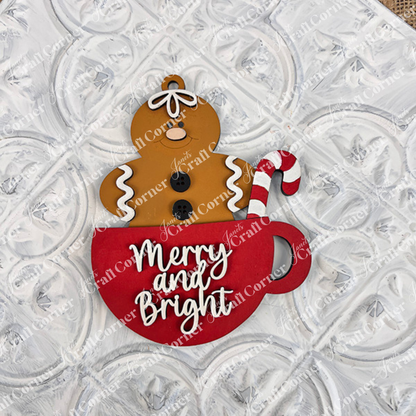 A smiling gingerbread figure sits in a red mug with a candy cane and "Merry and Bright" on the front—great holiday décor or inspiration for your next DIY holiday craft with Janet's Craft Corner's Gingerbread Ornaments kit (set of 8).