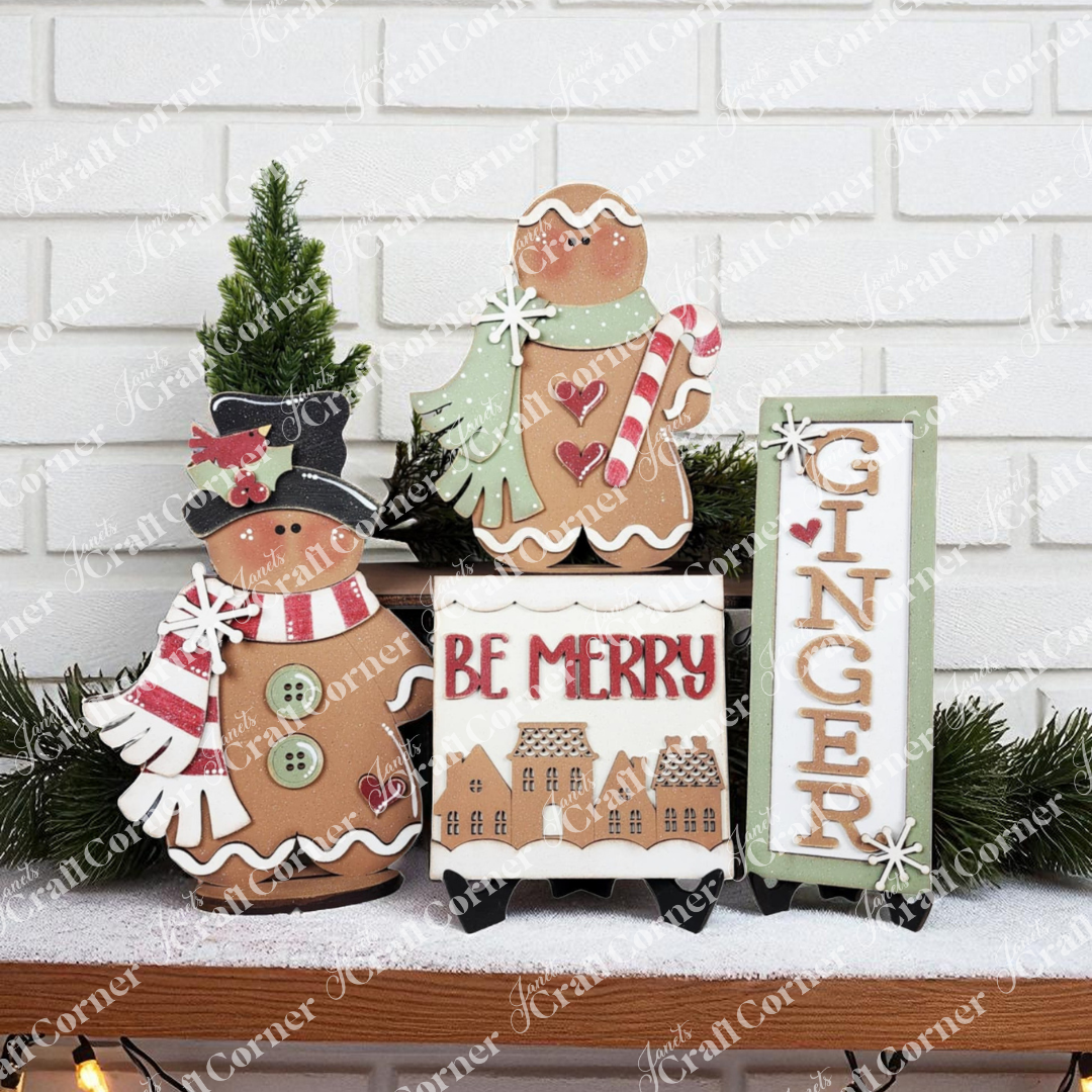 Janet's Craft Corner’s Gingerbread Mini Shelf Sitters DIY kit includes a snowman, gingerbread person with mint, and “GINGER” sign to create charming seasonal home decor amid greenery and “BE MERRY” blocks against a white brick wall.
