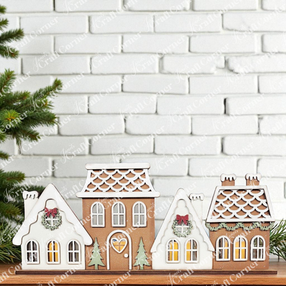 Janet's Craft Corner’s Gingerbread Village Votive Holder Shelf Sitter features three charming gingerbread-style houses with white icing details and wreaths, glowing warmly—perfect for festive, seasonal home decor.