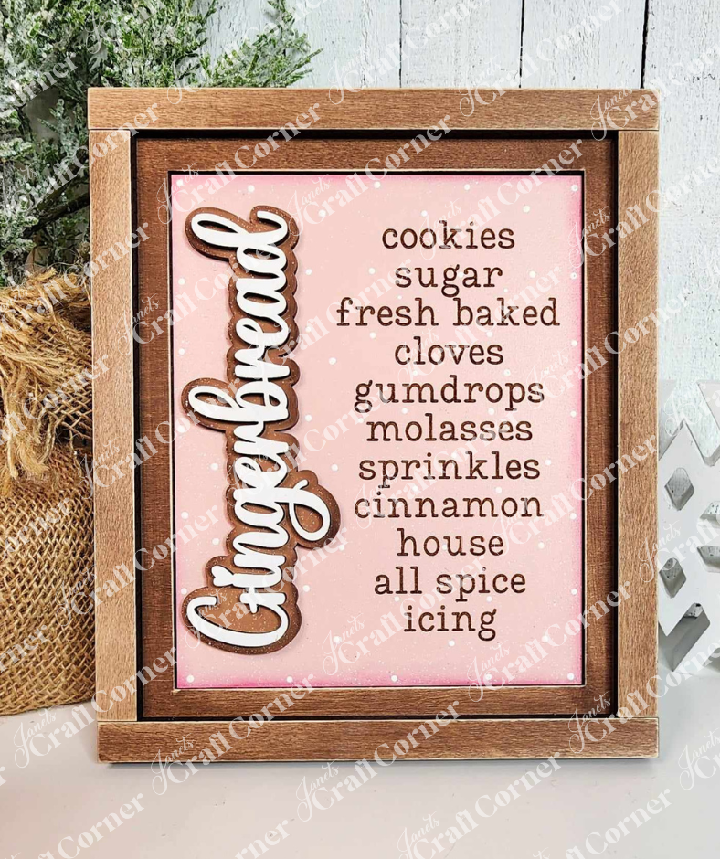 A painted sample of a sign from Janet's Craft Corner's Gingerbread Words Switchable Farmhouse Signs DIY home decor craft kit is displayed against a white shiplap wall. The sign features the word "Gingerbread" in cursive with words like cookies, cloves, cinnamon, and icing on a pink background—perfect seasonal home decor. 