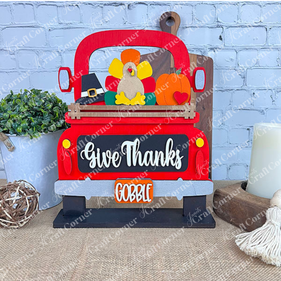 Introducing the DIY home decor kit from Janet's Craft Corner: an Antique Truck Base adorned with a hand-painted, colorful turkey, pumpkin, and pilgrim hat. The design features "Give Thanks" on the back and "Gobble" on the license plate. This piece is ideal for any interchangeable insert collection to celebrate different seasons or holidays.