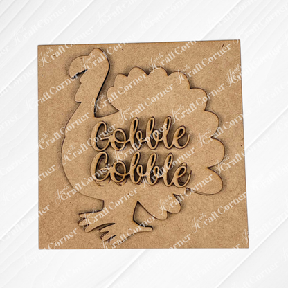 The Thanksgiving Feast Squares by Janet's Craft Corner feature a wood cut-out turkey with "Gobble Gobble" in cursive on a brown square—ideal as Swappable Squares or tiered tray decor for your seasonal display.