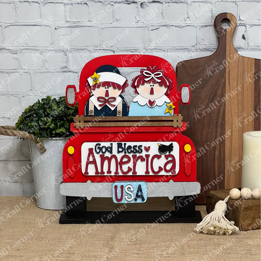 The God Bless America Interchangeable Insert by Janet's Craft Corner is a 3-piece DIY home decor kit featuring a wooden red truck with two cartoon people, "God Bless America," and a "USA" plate—perfect for your table with cutting boards, plants, or hay bale.