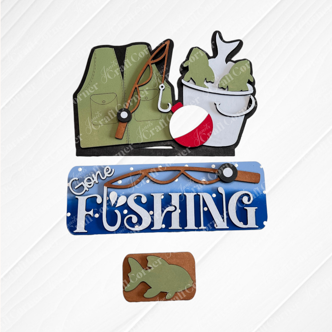 The Gone Fishing Interchangeable Insert DIY craft kit by Janet's Craft Corner includes 3 charming pieces—a green vest, fish bucket, and “Gone Fishing” sign—perfect for seasonal home decor.