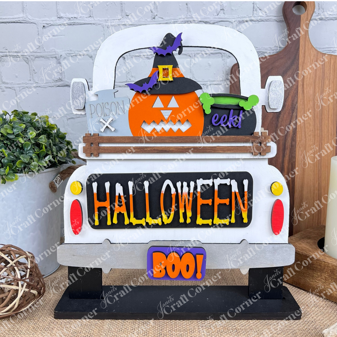 This delightful DIY home decor kit features Janet's Craft Corner's Halloween Pumpkin Interchangeable Insert, showcased on a truck with a cheerful pumpkin wearing a witch hat. The vibrant "HALLOWEEN" and "BOO!" text enhance its festive appeal. Accompanied by a plant, candle, and cutting boards set against a brick wall backdrop, it's ideal for those who enjoy interchangeable craft inserts.
