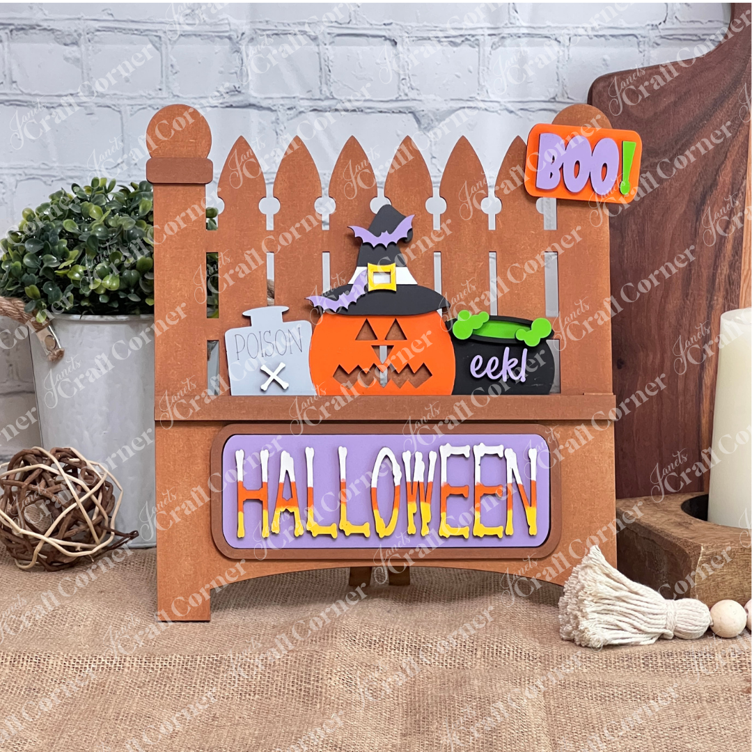 The Garden Fence with Insert from Janet's Craft Corner is a charming wooden Halloween decor featuring a picket fence design. It includes interchangeable elements like a pumpkin in a witch hat, "POISON" sign, green "eek!" cauldron, and colorful "BOO!" and "HALLOWEEN" signs, perfect for DIY lovers.
