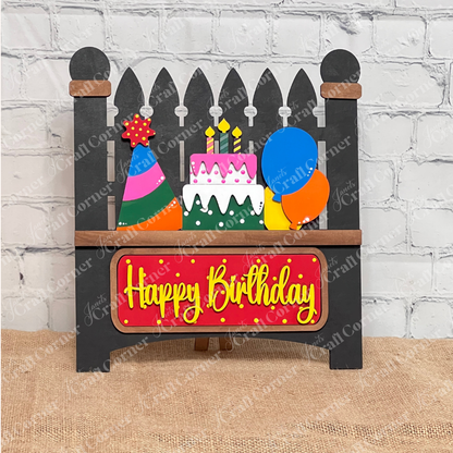 The Birthday Interchangeable Insert by Janet's Craft Corner features a wooden cake, candles, party hat, and balloons with "Happy Birthday" in yellow on a red background. Perfect for any birthday celebration, this DIY home decor craft kit includes a 3-piece set ideal for burlap surfaces against white brick walls.