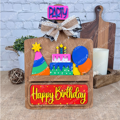 Janet's Craft Corner presents the "Birthday Interchangeable Insert," a delightful DIY home decor kit featuring a wooden board adorned with vibrant balloons, a party hat, and a cake complete with candles. The display is topped with a "Party" bow and showcases bold "Happy Birthday" letters below, making it an ideal addition to your interchangeable home decor or DIY craft kit collection.
