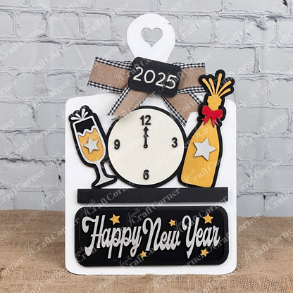 Janet's Craft Corner offers a DIY New Year decor kit, featuring a breadboard base with an insert showcasing a midnight clock, champagne bottle and glass accessories. The "Happy New Year" text is displayed with a bow on a brick wall backdrop, complete with a potted plant detail.