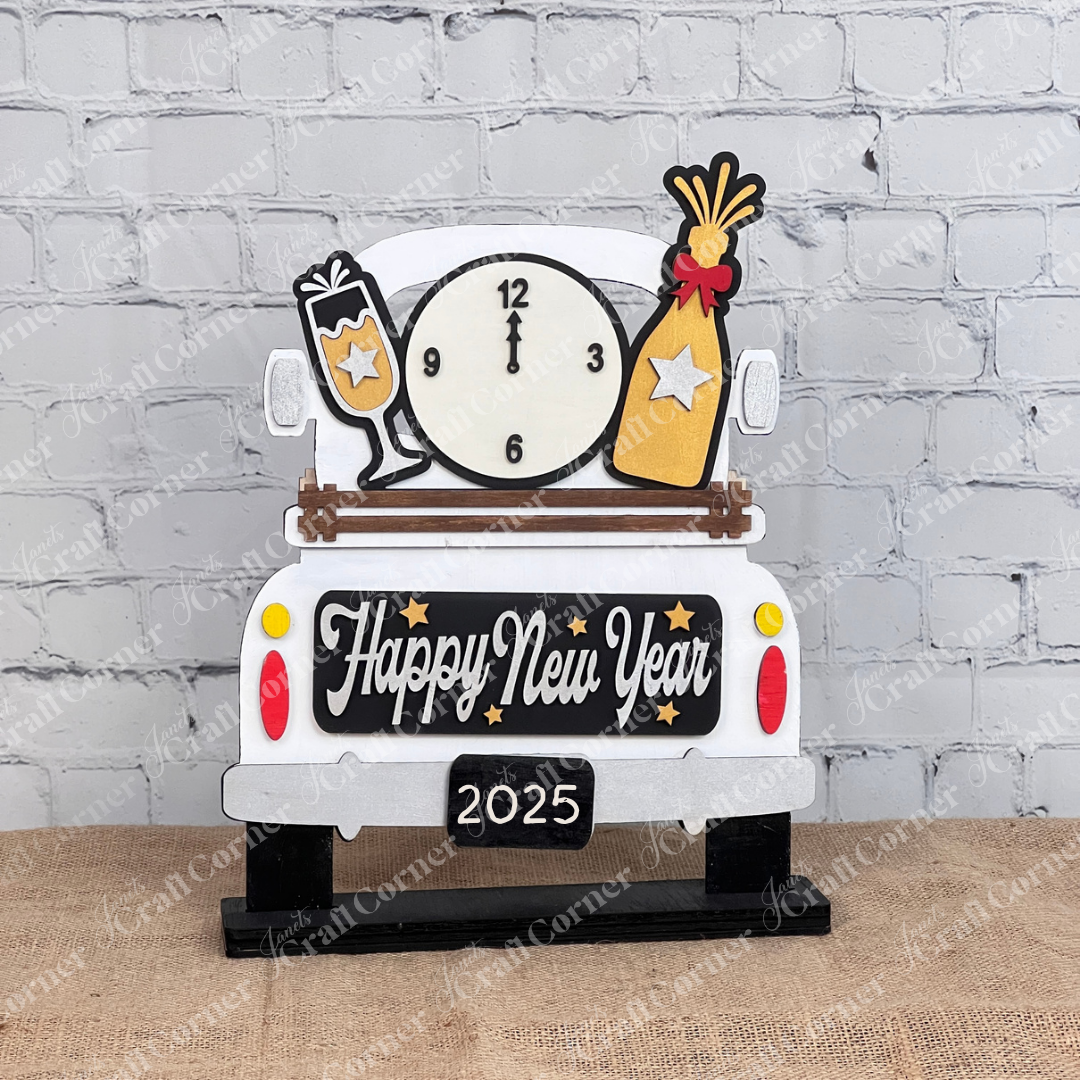 Unveil Janet's Craft Corner's DIY kit: an Antique Truck Base features "Happy New Year" on the back, adorned with a clock, champagne glass, and bottle. Perfect against a white brick wall with a potted plant and candle for versatile elegance.
