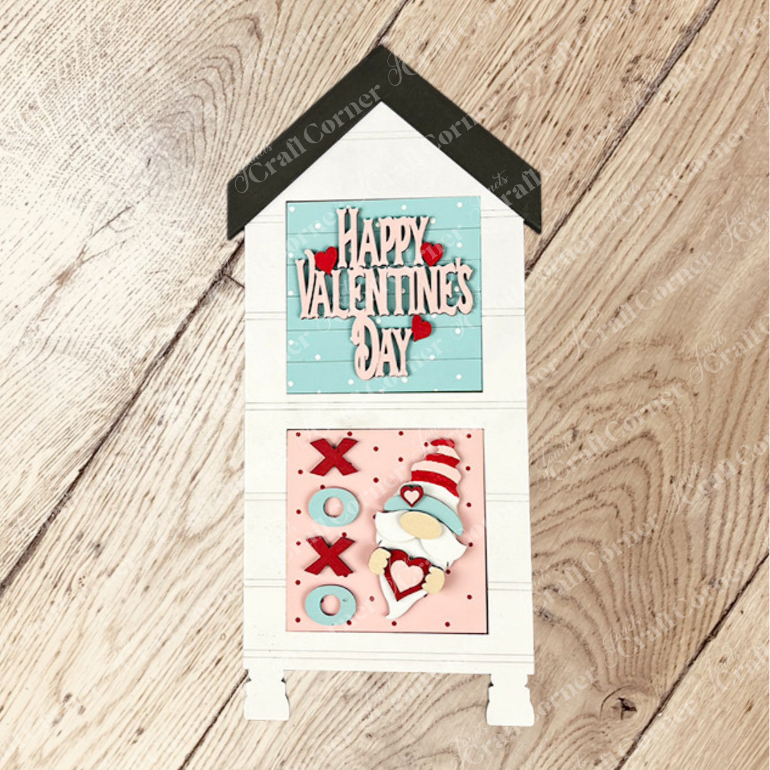 Janet's Craft Corner’s Valentine Squares features a house-shaped wooden sign that says "Happy Valentine's Day" on blue with hearts and a tic-tac-toe board with Xs, Os, and a gnome—perfect for charming DIY tiered tray home decor.