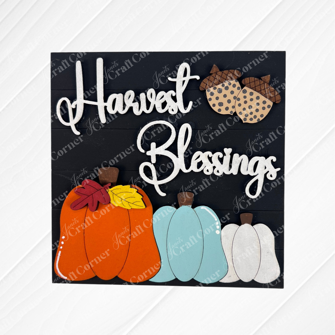 Janet's Craft Corner's "Harvest Blessings Thanksgiving Squares" is a decorative sign with "Harvest Blessings" in white script, two acorns on top, and colorful pumpkins with leaves on a dark background—ideal for tiered tray decor.