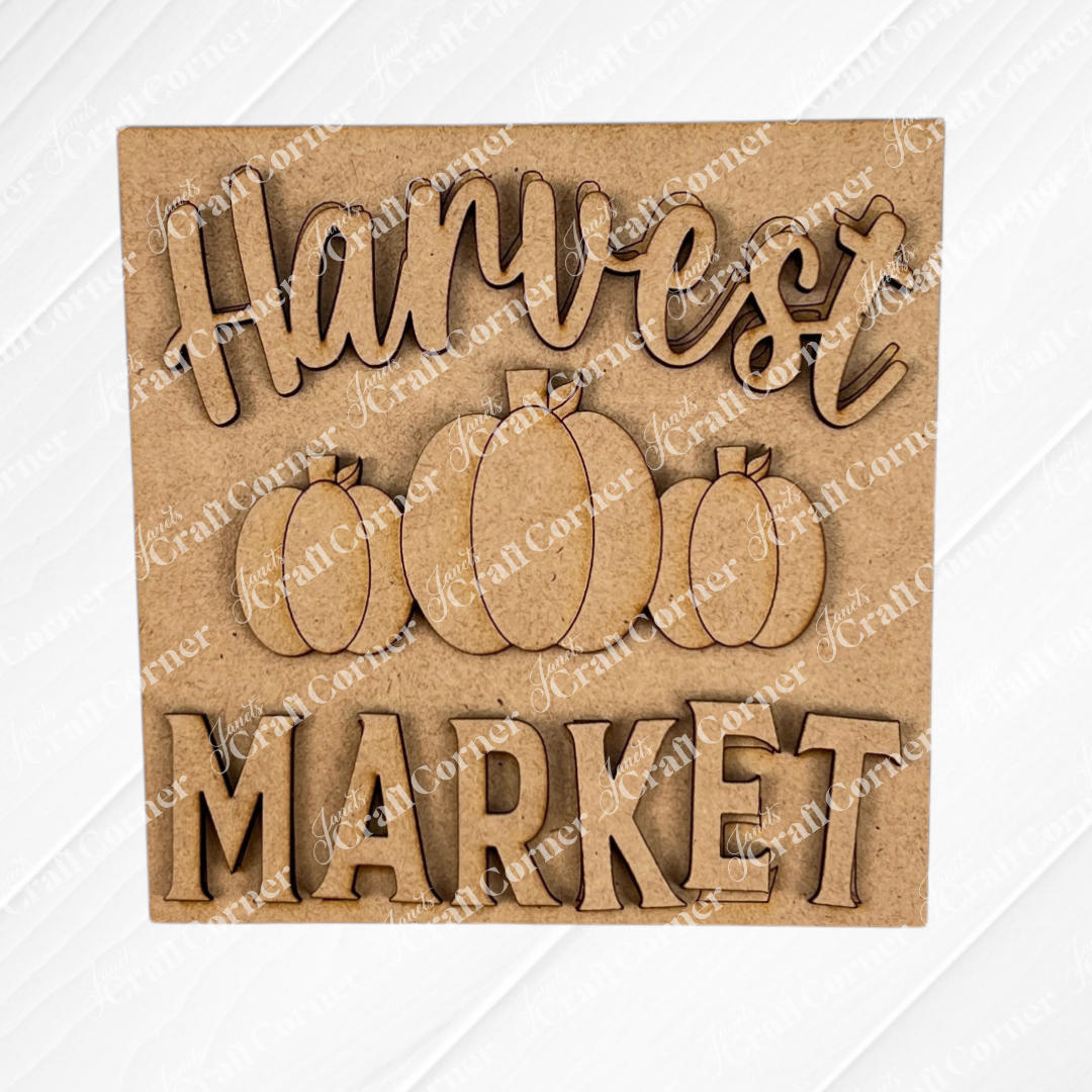 The "Hello Fall Squares" by Janet's Craft Corner features a wooden sign with laser-cut "Harvest Market" text and three engraved pumpkins. Perfect for tiered tray decor, it has a light wood background with a subtle diagonal white pattern.