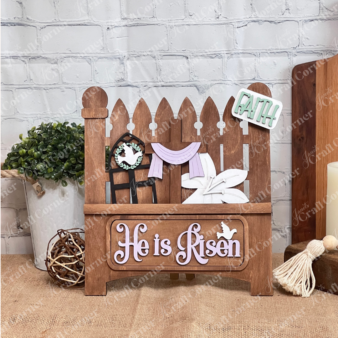 Add charm to your craft kit with Janet's Craft Corner DIY decor: a white picket fence featuring a rabbit with carrot, "EGGS 5¢" sign, colorful eggs, and "Hop" tag. Below, "Happy Easter" in purple and pink against a burlap and brick wall backdrop. 