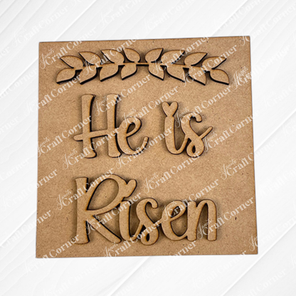 The Religious Easter Squares by Janet's Craft Corner feature a laser-cut "He is Risen" design with a leafy branch, ideal for tiered tray decor or paired with other cut-outs for a charming display. Set against a plain background.