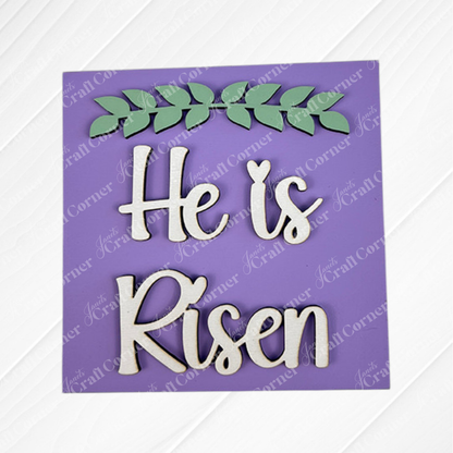The Religious Easter Squares by Janet's Craft Corner feature a purple sign with white cursive "He is Risen" and a green leafy branch—ideal for tiered trays or pairing with Swappable Squares.