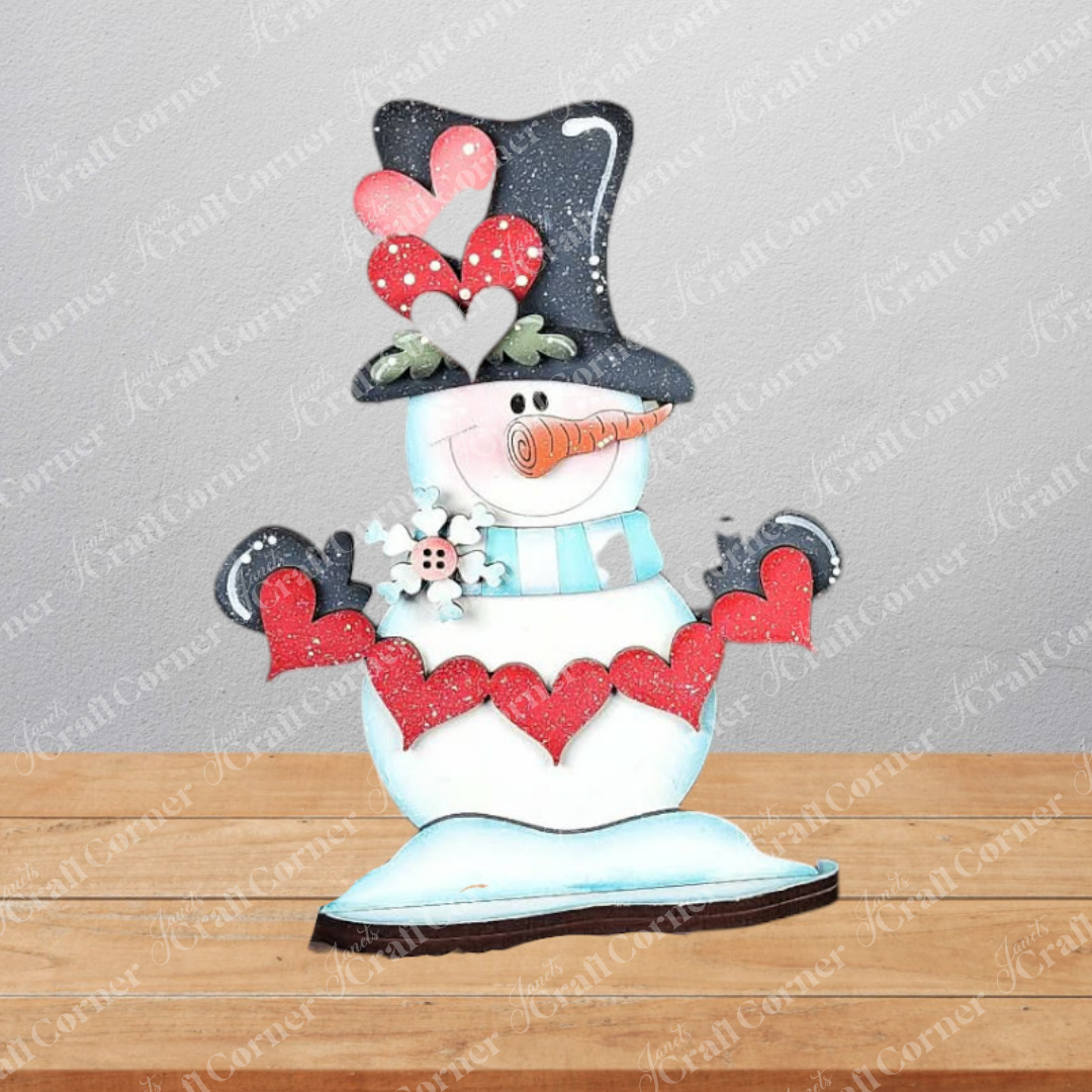 The Hearts Snowman Shelf Sitter by Janet's Craft Corner is a DIY seasonal home decor craft kit featuring a snowman with a black top hat, heart details, and blue scarf—perfect for festive shelves. Set of 1.