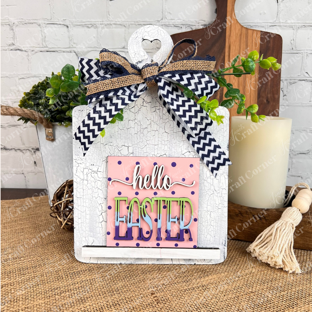 The "Hello Easter Squares" sign from Janet’s Craft Corner features a pink polka dot background and burlap bow, making it a charming decorative piece for Easter, perfect for craft kits or coffee-themed collections.