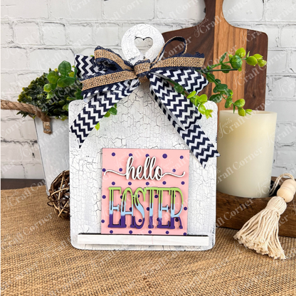 The "Hello Easter Squares" sign from Janet’s Craft Corner features a pink polka dot background and burlap bow, making it a charming decorative piece for Easter, perfect for craft kits or coffee-themed collections.