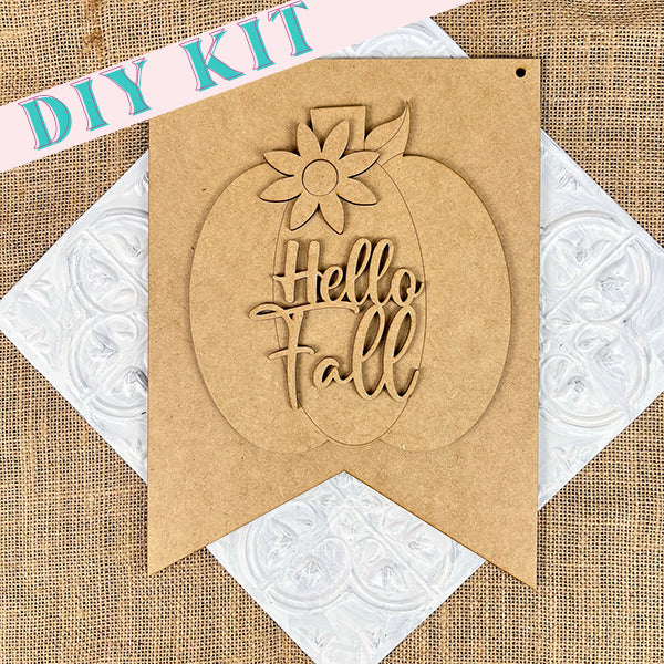 Janet's Craft Corner presents the Hello Fall Wall Hanger DIY kit, including a handcrafted door hanger with a cardboard pennant that highlights a pumpkin design and the phrase "Hello Fall." The piece features an appealing burlap-textured background, enhanced by decorative embossed paper accents, making it an ideal complement to your autumn decor.