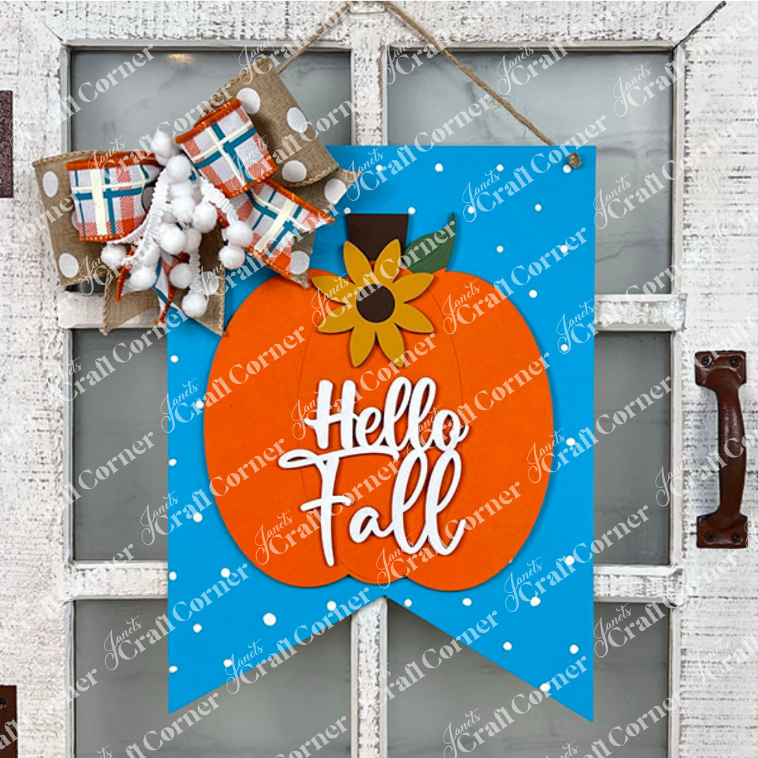 The "Hello Fall Wall Hanger" from Janet's Craft Corner is a handcrafted decoration featuring an orange pumpkin and a sunflower set against a blue background with white dots on a white door. With the text "Hello Fall," it's adorned with a large plaid and pom-pom bow, adding charm to any entrance this autumn.