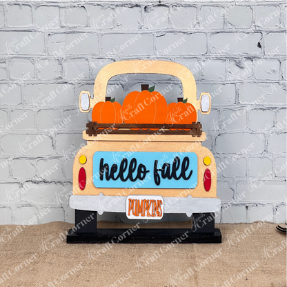 Introducing the "Hello Fall Interchangeable Insert" from Janet's Craft Corner—a charming DIY home decor kit featuring a sign shaped like a truck bed carrying orange pumpkins. With "hello fall" inscribed on the truck's blue tailgate and a "PUMPKINS" license plate, it's perfect for seasonal decoration. Pair it with items like a potted plant, cutting board, and candle for an extra touch of charm.
