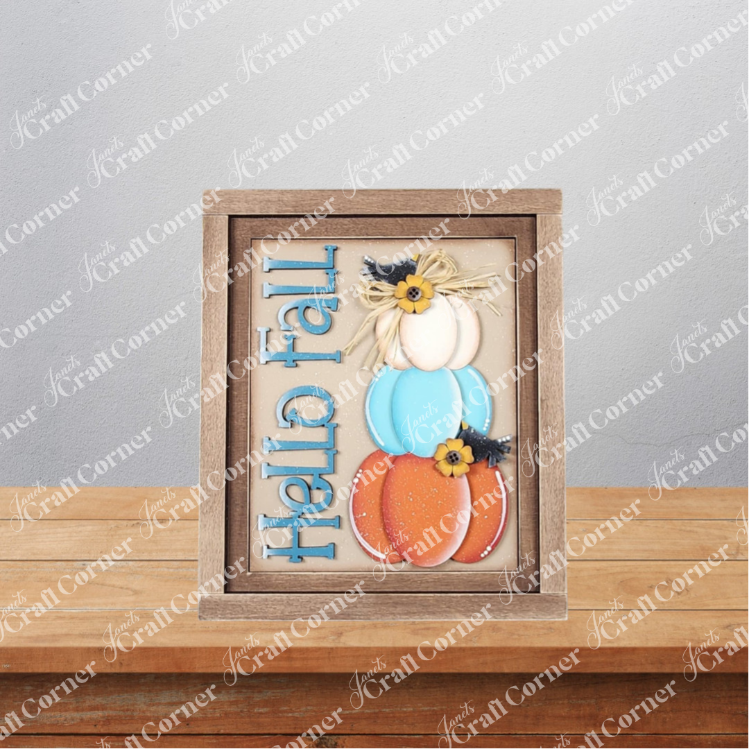 Janet's Craft Corner Fall Switchable Farmhouse Sign DIY kit features three stacked pumpkins in white, blue, and orange with "Hello Fall" in blue—perfect seasonal decor for your home. Choose from 9 designs; set of 1 included.