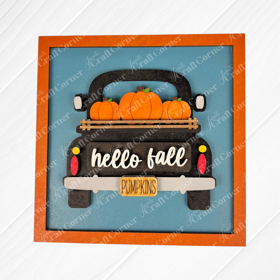 The Hello Fall Squares by Janet's Craft Corner features a decorative wood cut-out sign of a black truck with pumpkins, “hello fall” on the tailgate, and a yellow “PUMPKINS” license plate—ideal for tiered tray décor or Swappable Squares.