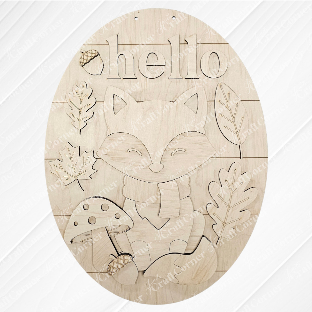 The Hello Fox Oval Door Hanger by Janet's Craft Corner is a DIY craft kit featuring a fox in a scarf, mushrooms, leaves, an acorn, and "hello"—perfect autumn decor for your door. Set of 1.