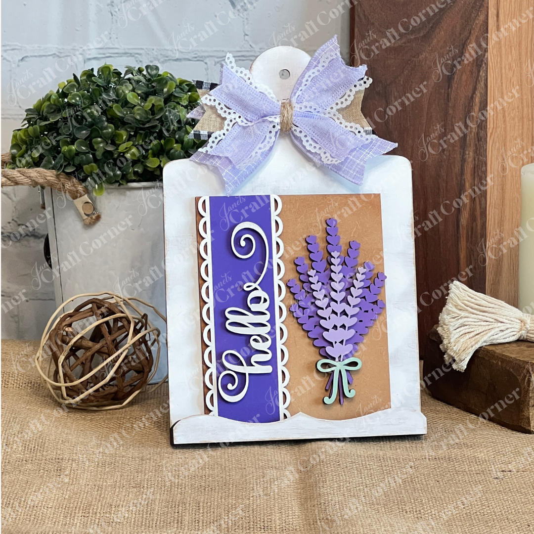 Janet's Craft Corner Lavender Switchable Farmhouse Signs DIY Craft Kit features a "Hello" card with purple accents, crafted lavender flowers, and a white-lavender bow. Ideal as tiered tray décor or a farmhouse sign on burlap surfaces.