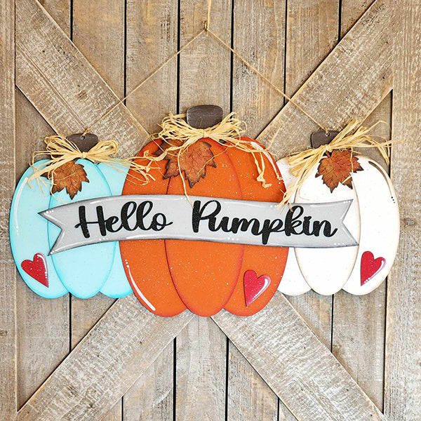 Introducing the "Hello Pumpkin Door Hanger" DIY home decor kit by Janet's Craft Corner. This charming craft kit includes three hand-painted pumpkins in turquoise, orange, and white, each embellished with a leaf and straw bow. The pumpkins are arranged with a banner that reads "Hello Pumpkin" against a rustic wooden backdrop.