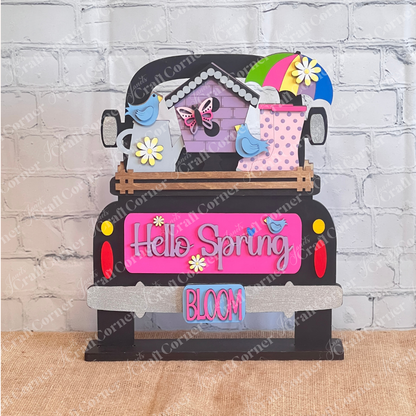 Introducing Janet's Craft Corner's DIY Home Decor Kit: an Antique Truck Base with Interchangeable Insert, perfect for welcoming spring. This vibrant design includes a "Hello Spring" sign adorned with bright purple, pink, and green colors. It features delightful hand-painted elements like flowers, birds, a butterfly, an umbrella, and a polka dot watering can. Ideal for crafting enthusiasts who enjoy creating their own decorative door hangings.