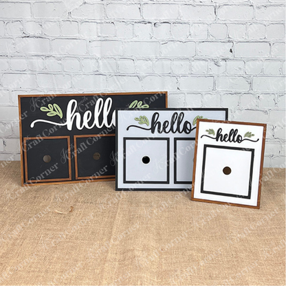 Three "Hello Swappable Squares Holder" DIY Craft Kits by Janet's Craft Corner, in black, gray, and white, sit on burlap and feature painted leaves with two spaces for seasonal inserts.