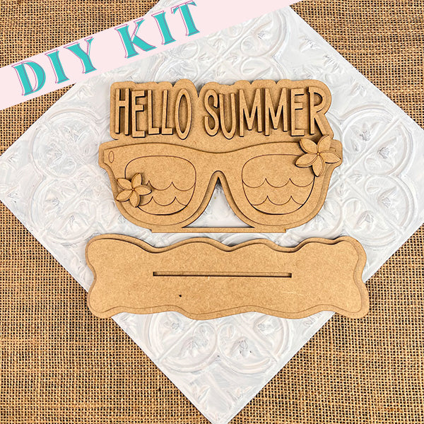 This shelf sitter from Janet's Craft Corner features a delightful wooden cutout in the shape of sunglasses, adorned with the phrase "HELLO SUMMER" at the top. Ideal for beachy farmhouse decor, it includes floral designs and a wavy accent underneath against a textured backdrop.