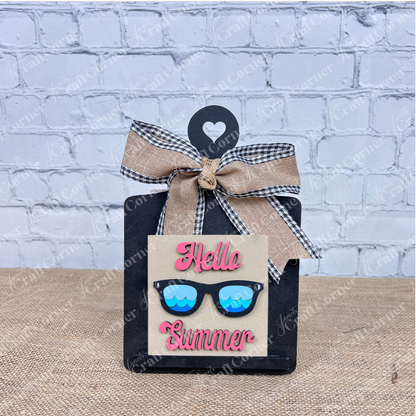 Add a pop of color to your home with the Summer Lovin Swappable Squares DIY craft kit from Janet's Craft Corner—featuring "Hello Summer" in pink, blue sunglasses wood cut-outs, and a burlap plaid bow for eye-catching seasonal decor.