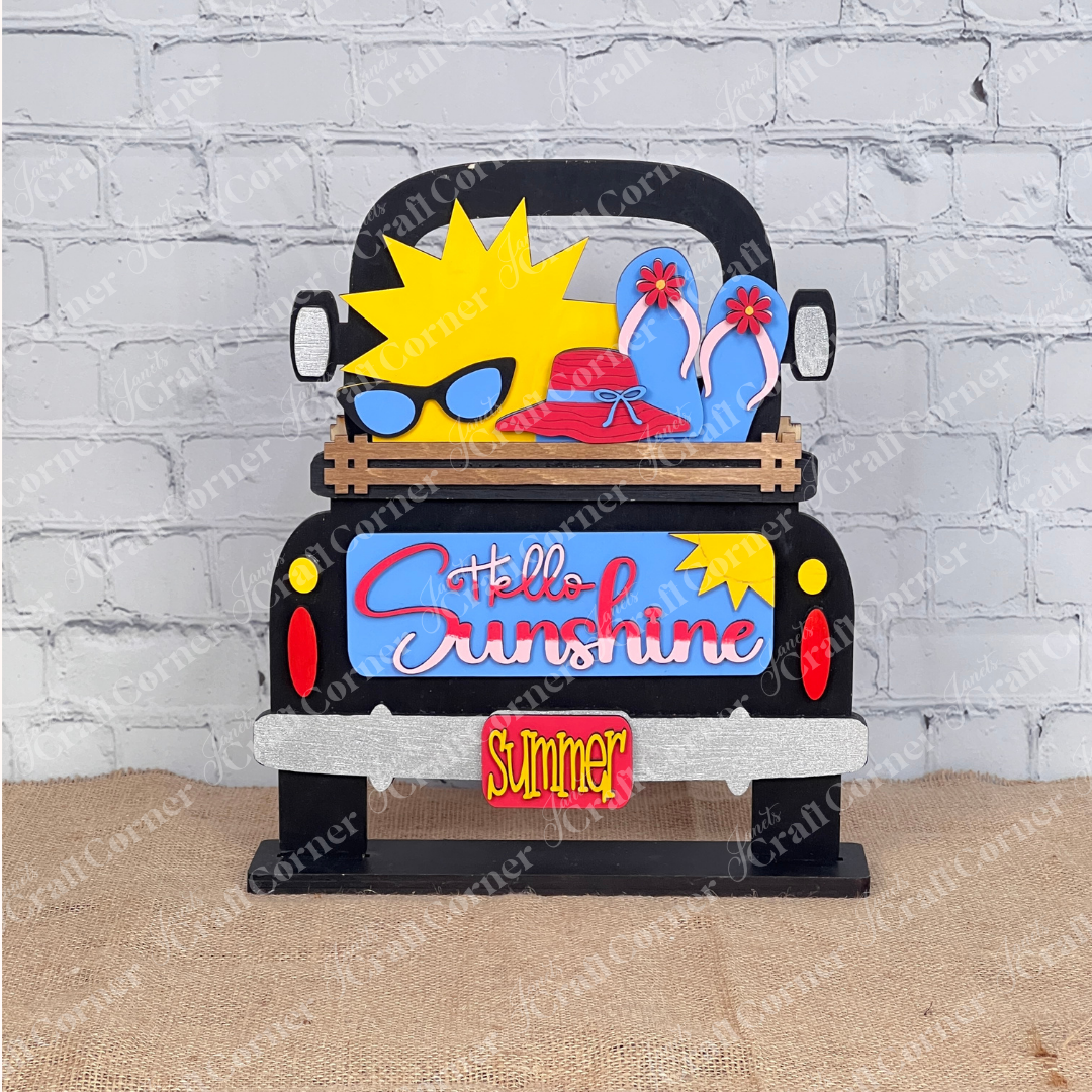 The "Antique Truck Base with Insert" from Janet's Craft Corner is a charming DIY decor kit featuring an antique truck sign with "Hello Sunshine" and "Summer." It showcases a sun with sunglasses, a pink hat, blue flip-flops, and backgrounds like brick walls and cutting boards for added flair.