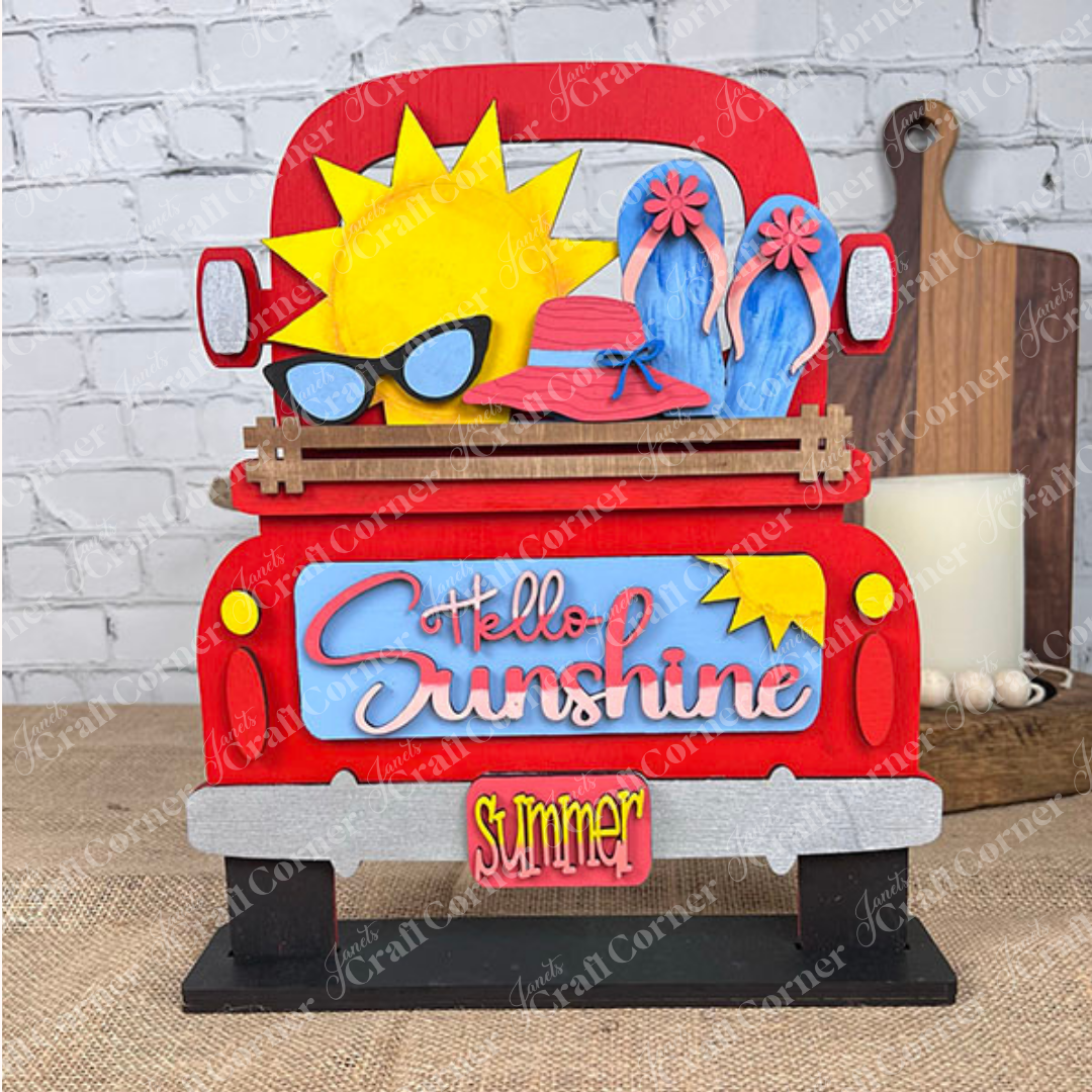 The Hello Sunshine Interchangeable Insert from Janet's Craft Corner is a hand-painted DIY home decor kit featuring a decorative red truck adorned with summer-themed elements: a large sun sporting sunglasses, a pink hat, blue flip-flops, and the phrases "Hello Sunshine" and "Summer" on the back. This charming piece makes an ideal addition to any brick wall backdrop for home decor enthusiasts.