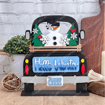 Janet's Craft Corner presents the Antique Truck Base with Insert, a DIY interchangeable home decor kit featuring a decorative wood cutout of an antique truck with a snowman, trees, and snowflakes. "Hello Winter" and "Brrr" phrases complete this charming seasonal piece against rustic brick and burlap.